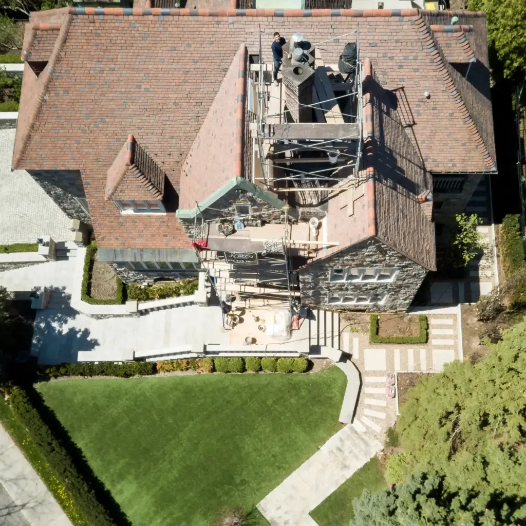Aerial view of a historic stone home undergoing masonry restoration, with scaffolding set up for chimney and facade repairs.
